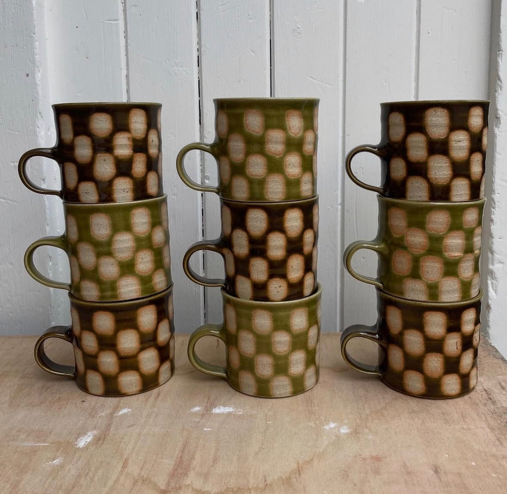 A stack of Edmund Davies checkerboard mugs in green and brown glazes