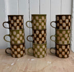 A stack of Edmund Davies checkerboard mugs in green and brown glazes