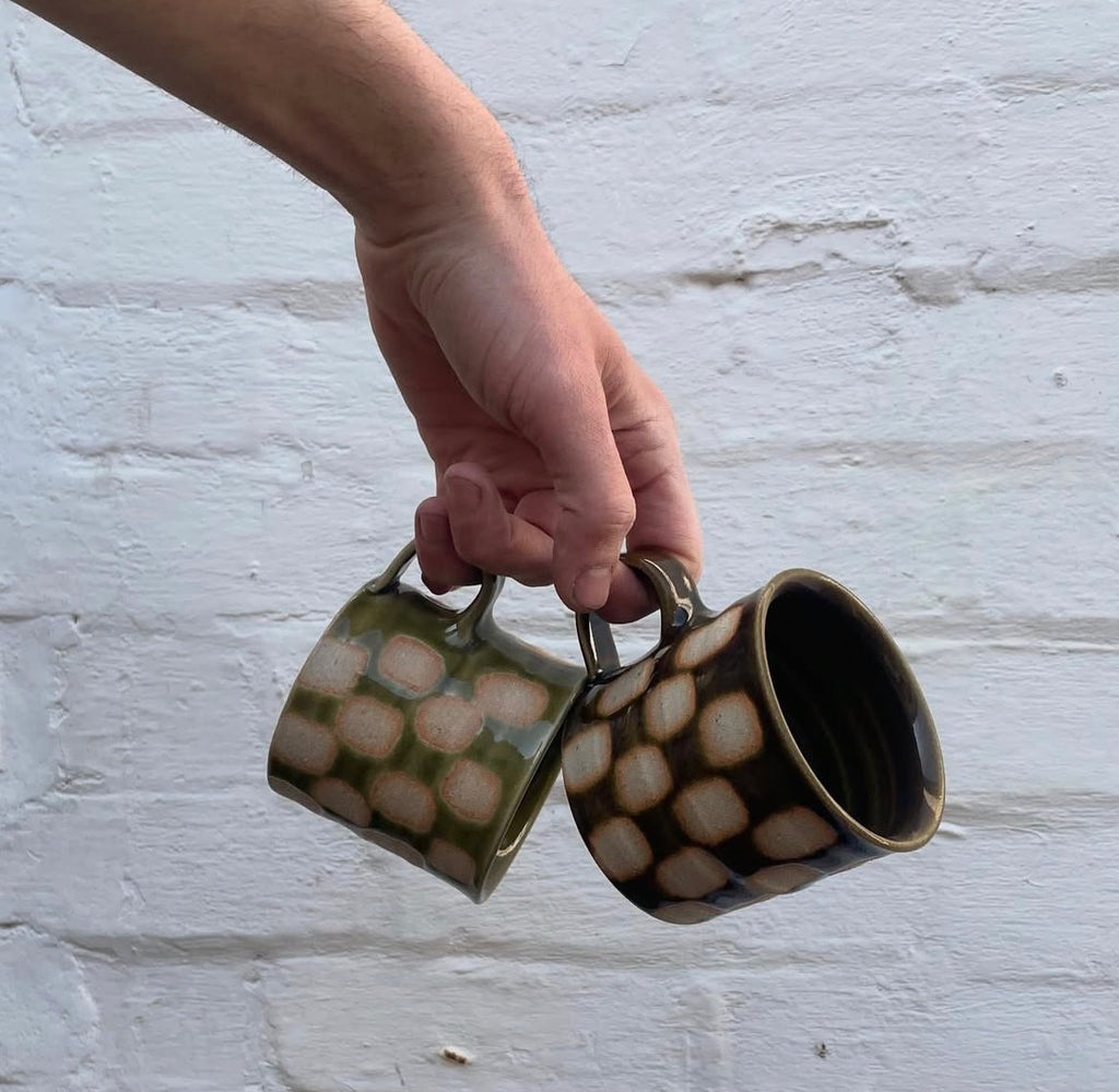 Two checkerboard mugs, one green and one brown, held by their low handles