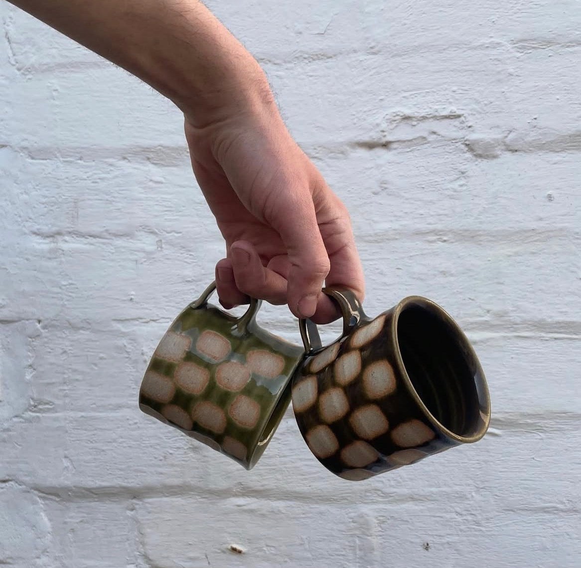 Two checkerboard mugs, one green and one brown, held by their low handles
