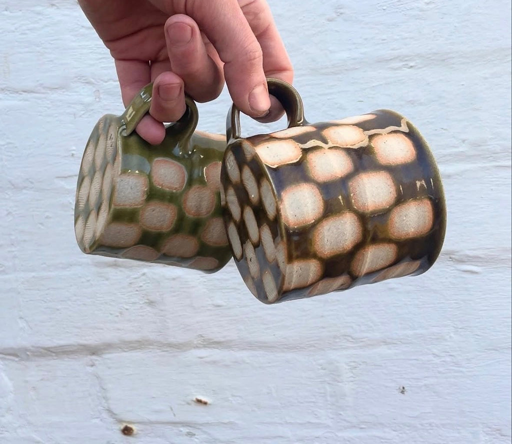 Green and brown checkerboard mugs held by their handles, showing the wax resist pattern