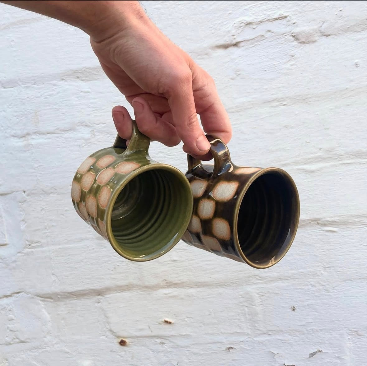 Looking into a green and a brown glossy-glazed checkerboard mug