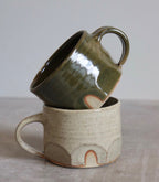 A green and a cream speckled glazed mug by Hannah Burgess Ceramics, stacked
