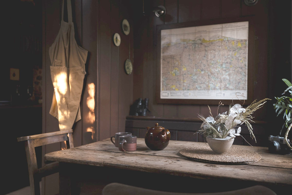 Timber-panelled room at Spinks Nest in North Norfolk with a rustic table, brown teapot, mugs, dried flowers and a framed map