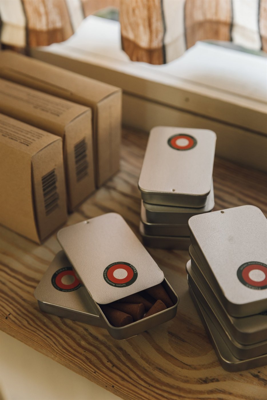 Slide-top tins of Foras incense cones in Juniper, Rosemary and Oud on a wooden shelf