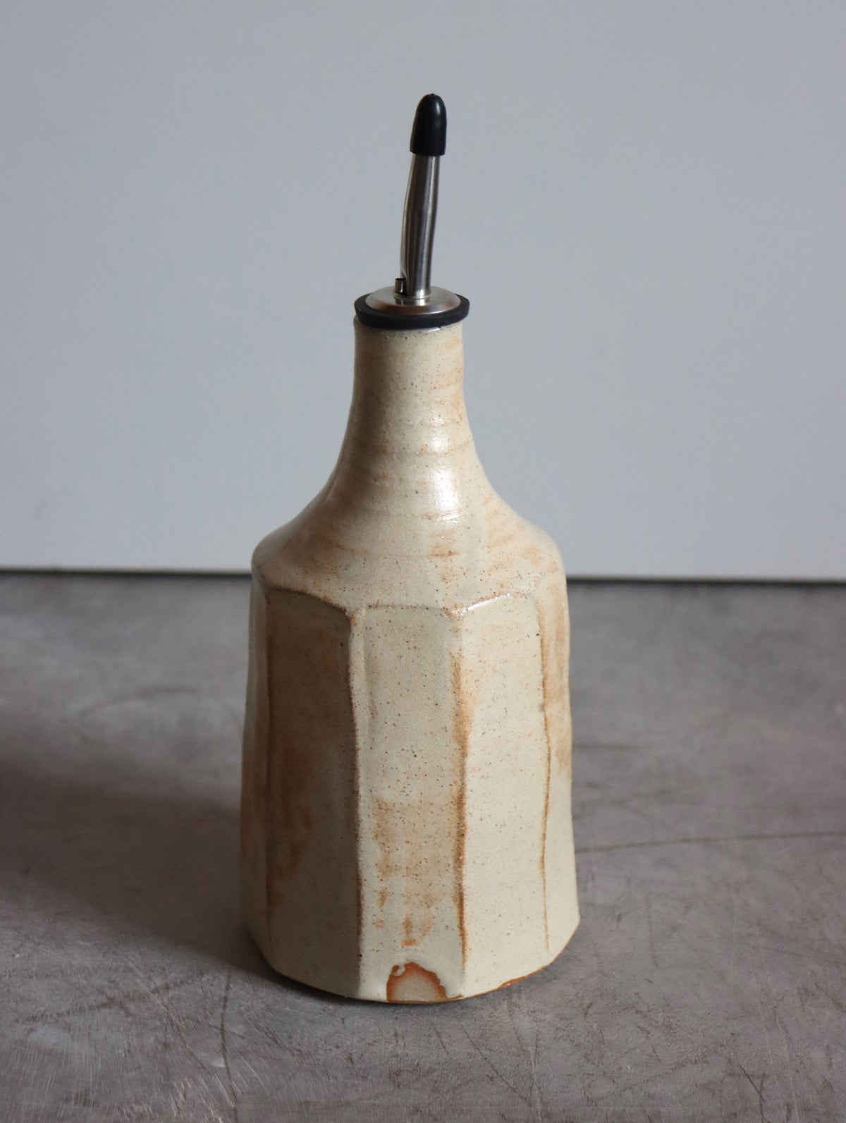 Faceted large oil pourer in iron-rich speckled white glaze with a steel pouring spout